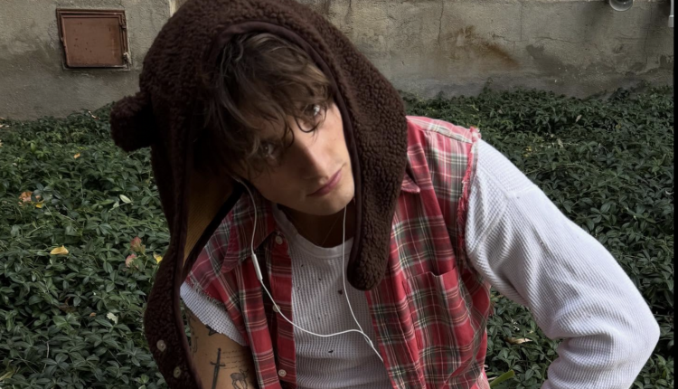 Thomas day looking down at the floor while wearing a flannel and a brown hoodie.